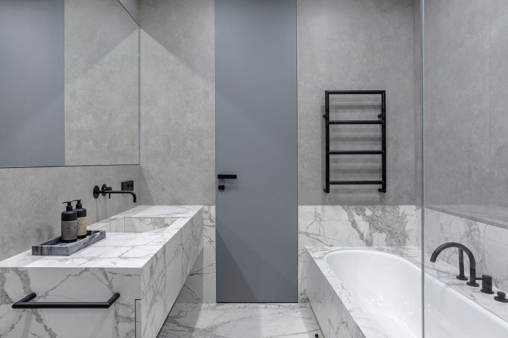 Ispirazione per una stanza da bagno minimal con ante lisce, ante grigie, vasca da incasso, piastrelle grigie, lavabo integrato, pavimento grigio e top grigio