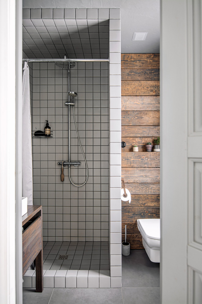 Idéer för att renovera ett litet nordiskt brun brunt badrum med dusch, med en dusch i en alkov, en vägghängd toalettstol, grå kakel, keramikplattor, grå väggar, klinkergolv i porslin, ett fristående handfat, träbänkskiva, grått golv och dusch med duschdraperi
