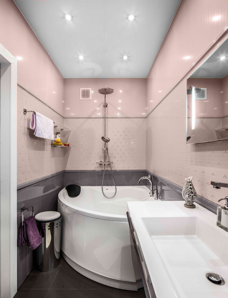 На фото: узкая и длинная ванная комната в современном стиле с угловой ванной, душем над ванной, розовой плиткой, серой плиткой, монолитной раковиной и серым полом с