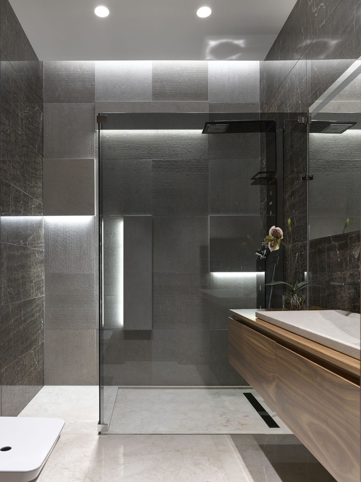 Bild på ett mellanstort funkis badrum med dusch, med släta luckor, skåp i mellenmörkt trä, grå kakel, porslinskakel, marmorgolv, ett nedsänkt handfat, träbänkskiva och en öppen dusch
