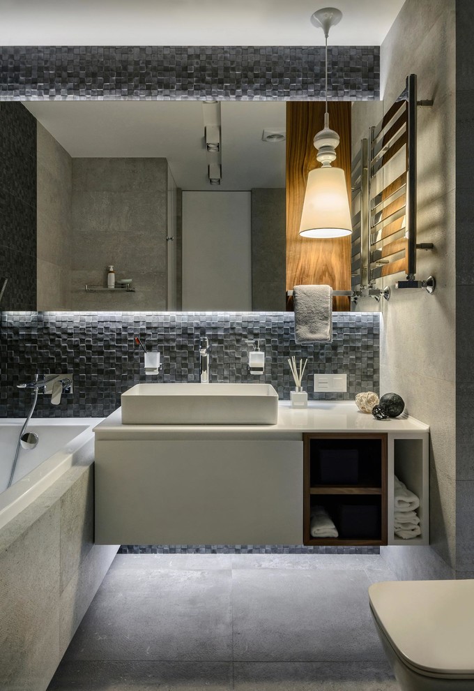 Bild på ett funkis en-suite badrum, med släta luckor, vita skåp, ett badkar i en alkov, grå kakel, ett fristående handfat, grått golv, en vägghängd toalettstol, mosaik, grå väggar, betonggolv och med dusch som är öppen