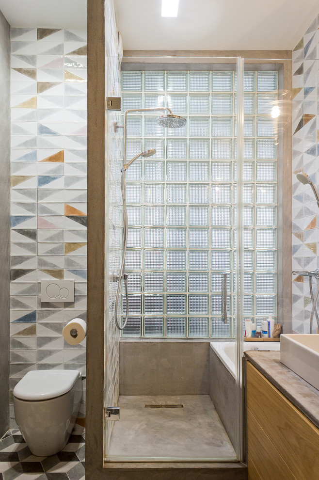 Inredning av ett industriellt badrum med dusch, med ett badkar i en alkov, våtrum, en toalettstol med separat cisternkåpa, flerfärgad kakel, ett fristående handfat, grått golv och dusch med gångjärnsdörr