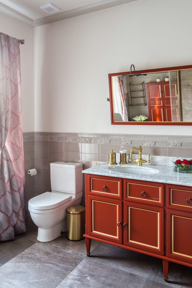 Cette image montre une salle de bain traditionnelle de taille moyenne avec des portes de placard rouges, un carrelage beige, des carreaux de porcelaine, un mur blanc, un sol en carrelage de porcelaine, un lavabo encastré, un plan de toilette en marbre, WC séparés et un placard avec porte à panneau encastré.