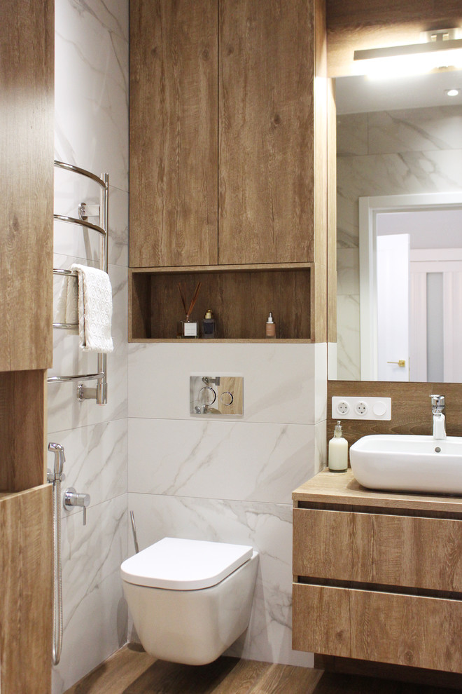 Modelo de cuarto de baño actual con armarios con paneles lisos, puertas de armario de madera oscura, sanitario de pared, lavabo sobreencimera y suelo marrón