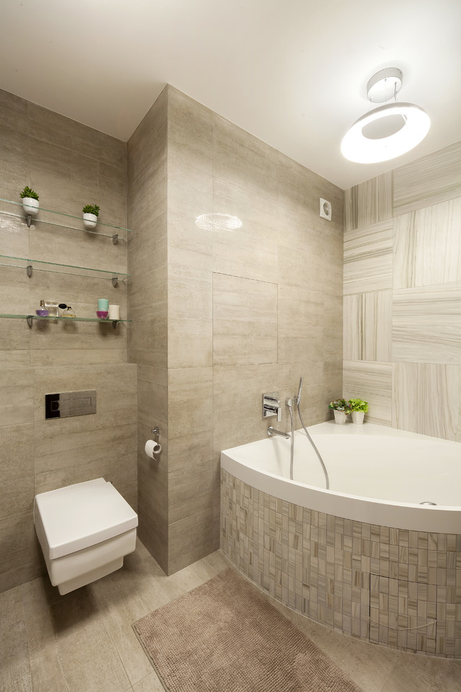 Modern inredning av ett badrum, med ett hörnbadkar, en vägghängd toalettstol och beige kakel