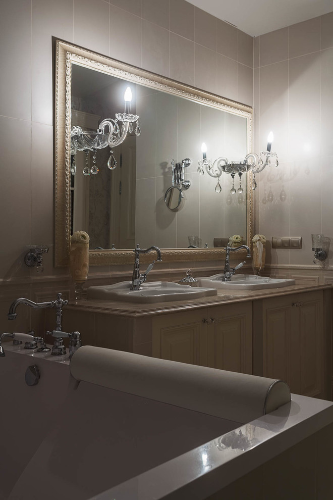 На фото: главная ванная комната в классическом стиле с фасадами с выступающей филенкой, бежевыми фасадами, полновстраиваемой ванной, бежевой плиткой, бежевыми стенами и накладной раковиной