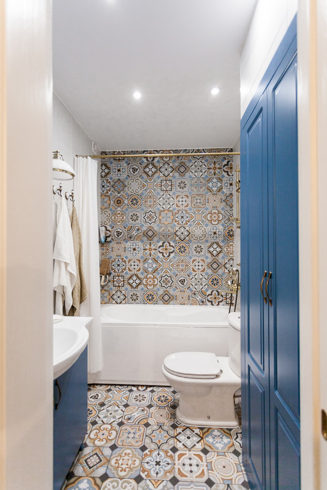 Medelhavsstil inredning av ett litet vit vitt badrum med dusch, med ett badkar i en alkov, en dusch/badkar-kombination, grå kakel, porslinskakel, vita väggar, flerfärgat golv, dusch med duschdraperi, luckor med upphöjd panel, blå skåp, en toalettstol med separat cisternkåpa, cementgolv och ett integrerad handfat