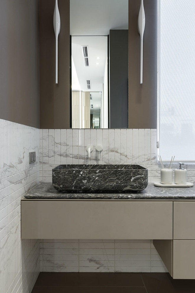 Réalisation d'une salle de bain design avec du carrelage en marbre, un plan de toilette en marbre, un plan de toilette gris, un mur marron, un placard à porte plane, des portes de placard marrons, un carrelage blanc, une vasque et un sol marron.