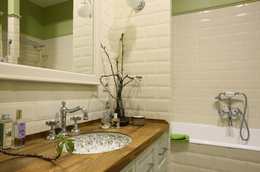 Bild på ett lantligt badrum, med vita skåp, ett badkar i en alkov, en dusch/badkar-kombination, beige kakel, tunnelbanekakel, gröna väggar, ett undermonterad handfat och träbänkskiva
