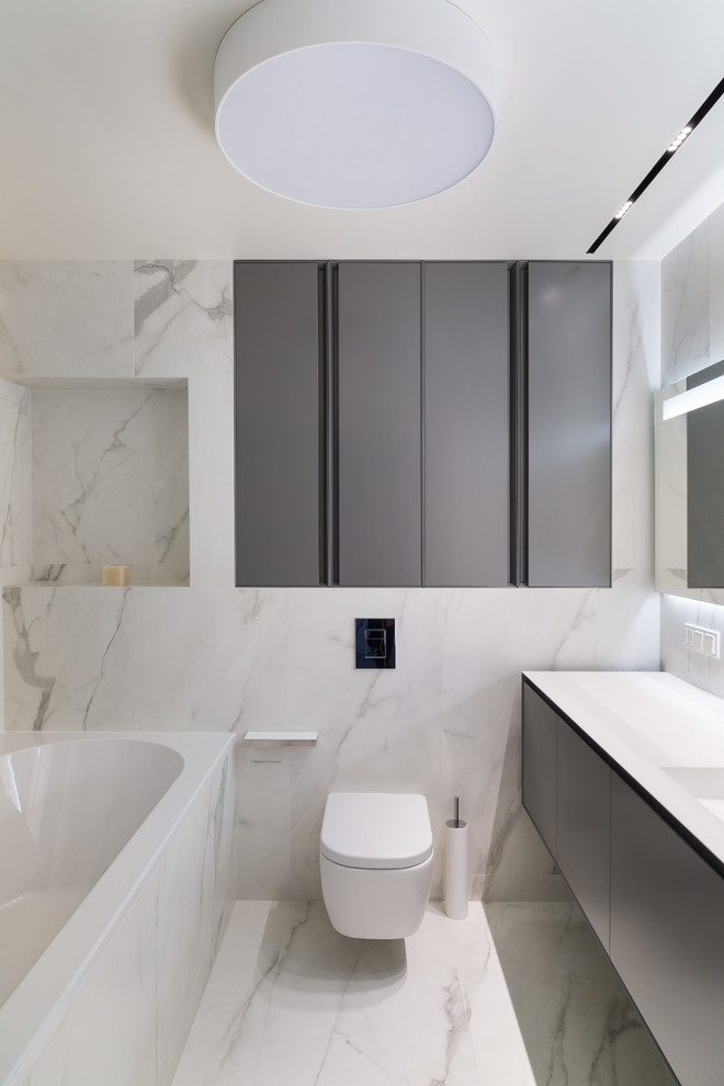 Exemple d'une salle de bain principale et grise et blanche scandinave avec un placard à porte plane, des portes de placard noires, WC suspendus, un carrelage blanc, un lavabo intégré et une baignoire en alcôve.