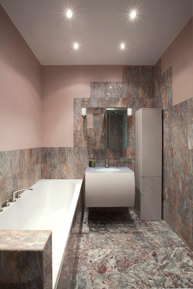 На фото: главная ванная комната среднего размера в современном стиле с плоскими фасадами, угловым душем, розовой плиткой, каменной плиткой, розовыми стенами, мраморным полом, стеклянной столешницей, серыми фасадами, накладной ванной и врезной раковиной