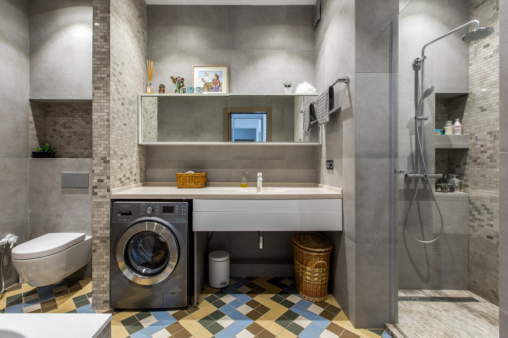 Modernes Badezimmer mit weißen Schränken, Duschnische, grauen Fliesen, Unterbauwaschbecken, buntem Boden, beiger Waschtischplatte und Wäscheaufbewahrung in Sonstige
