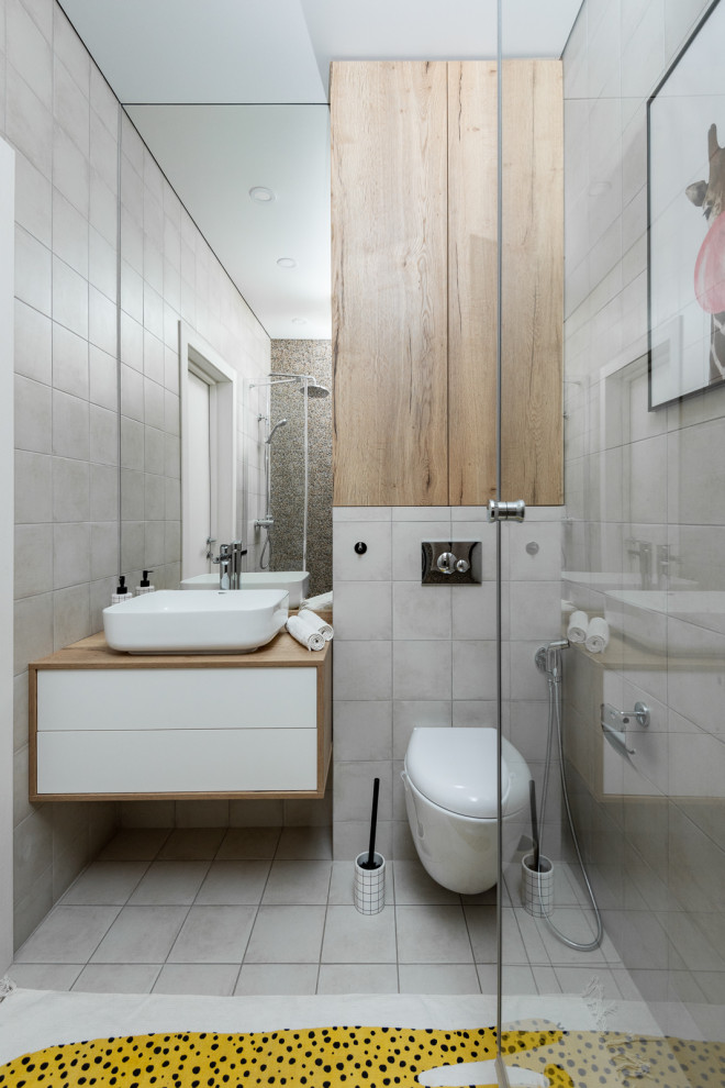 Idéer för att renovera ett mellanstort funkis beige beige badrum med dusch, med släta luckor, vita skåp, grå kakel, porslinskakel, klinkergolv i porslin, ett fristående handfat, träbänkskiva och grått golv
