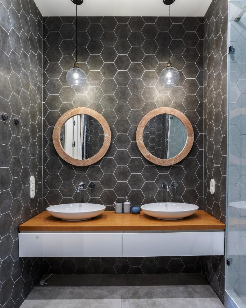 Modern inredning av ett mellanstort brun brunt badrum med dusch, med släta luckor, vita skåp, grå kakel, ett fristående handfat, träbänkskiva och grått golv