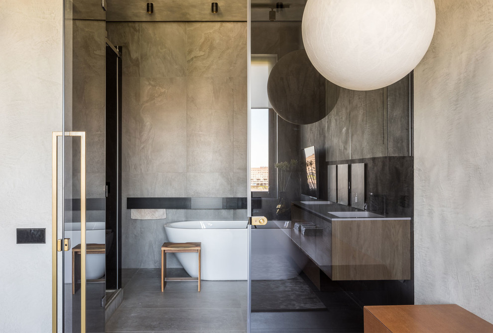 Inspiration for an urban ensuite bathroom in Saint Petersburg with a freestanding bath, grey walls, grey floors, flat-panel cabinets, medium wood cabinets, an alcove shower, grey tiles, concrete flooring, a submerged sink and a hinged door.