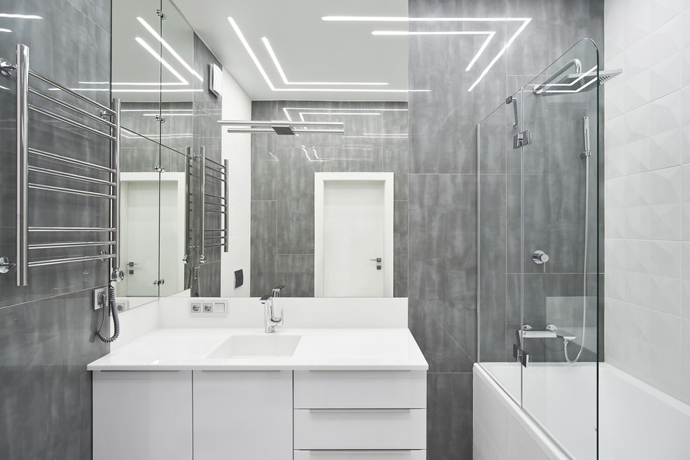 Inspiration för ett mellanstort funkis vit vitt en-suite badrum, med släta luckor, vita skåp, ett undermonterat badkar, en dusch/badkar-kombination, grå kakel, porslinskakel, grå väggar, ett undermonterad handfat, bänkskiva i akrylsten och dusch med gångjärnsdörr
