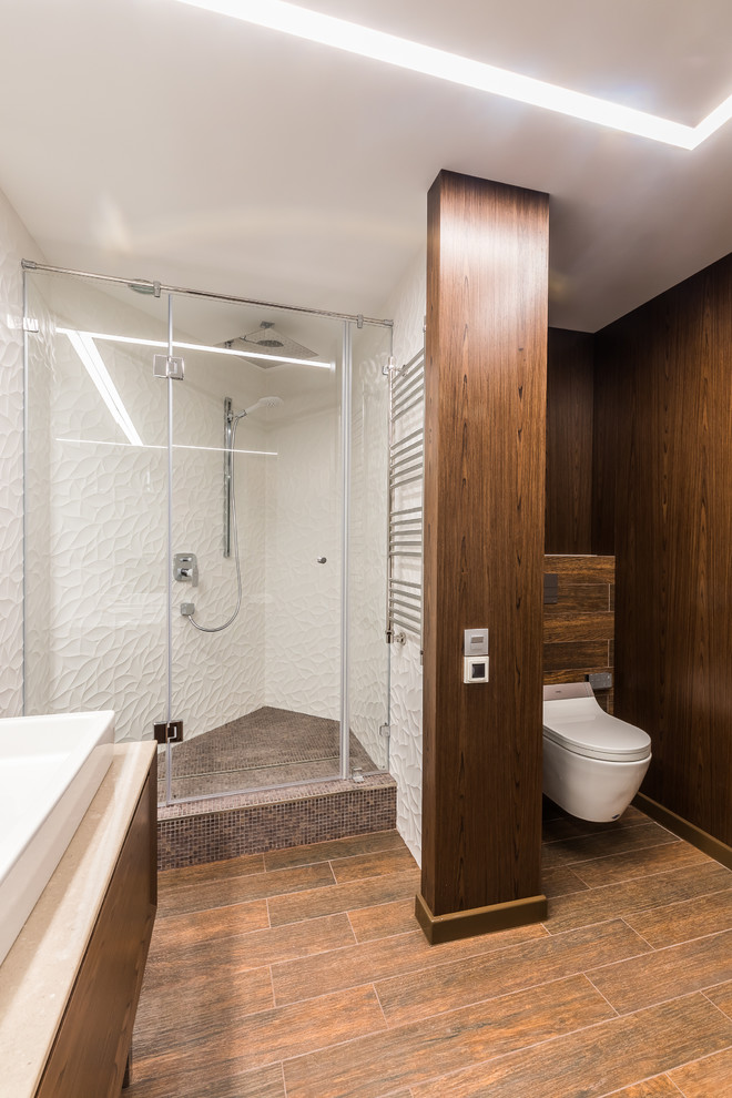 Photo of a contemporary shower room bathroom in Other with a corner shower, a wall mounted toilet, brown floors, a hinged door, flat-panel cabinets, dark wood cabinets, white tiles and a vessel sink.