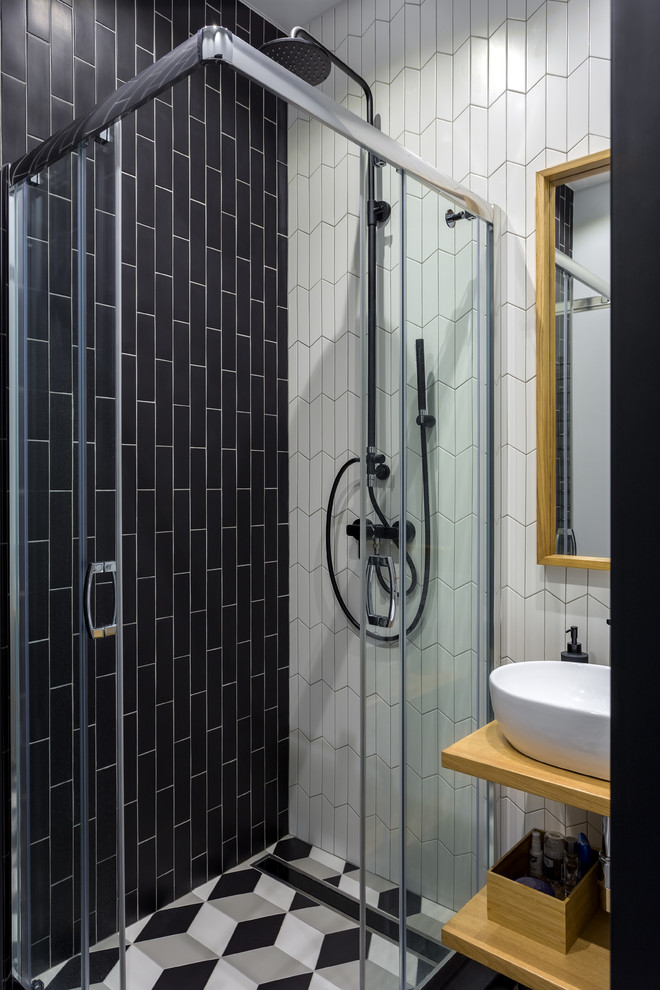 Nordisk inredning av ett litet badrum med dusch, med öppna hyllor, skåp i ljust trä, en hörndusch, keramikplattor, klinkergolv i keramik, träbänkskiva, flerfärgat golv, dusch med skjutdörr, vit kakel, svart kakel och ett fristående handfat