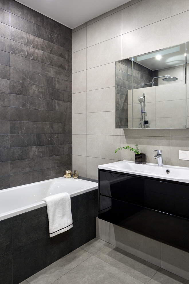 Пример оригинального дизайна: главная ванная комната среднего размера в современном стиле с плоскими фасадами, черными фасадами, полновстраиваемой ванной, душевой комнатой, инсталляцией, черной плиткой, керамической плиткой, серыми стенами, полом из керамической плитки, накладной раковиной, серым полом и душем с распашными дверями