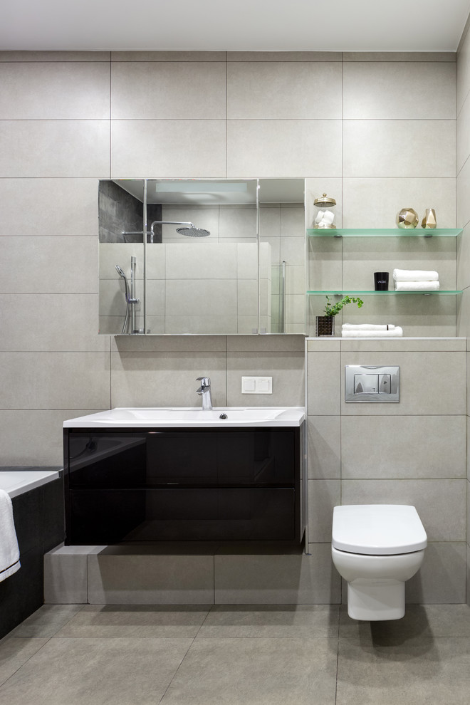 Photo of a medium sized contemporary ensuite wet room bathroom in Moscow with flat-panel cabinets, black cabinets, a submerged bath, a wall mounted toilet, black tiles, ceramic tiles, grey walls, ceramic flooring, a built-in sink, grey floors and a hinged door.