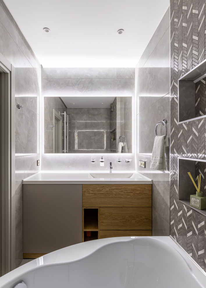 Пример оригинального дизайна: ванная комната среднего размера в современном стиле с плоскими фасадами, светлыми деревянными фасадами, гидромассажной ванной, душем над ванной, серой плиткой, душевой кабиной, монолитной раковиной, открытым душем и белой столешницей