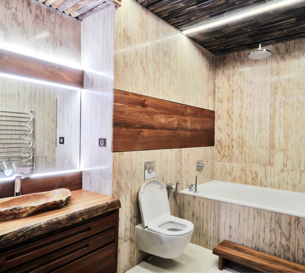 На фото: главная ванная комната в современном стиле с темными деревянными фасадами, ванной в нише, инсталляцией, бежевой плиткой, настольной раковиной и столешницей из дерева