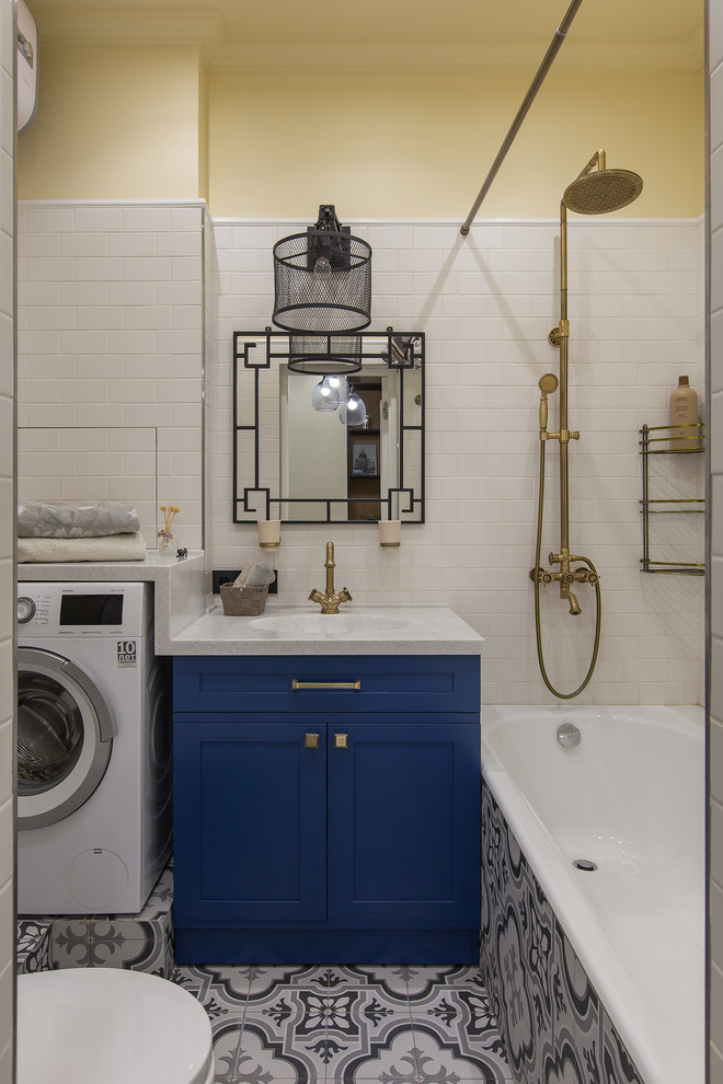 На фото: главная ванная комната в современном стиле с фасадами с утопленной филенкой, синими фасадами, ванной в нише, душем над ванной, белой плиткой, желтыми стенами, разноцветным полом, шторкой для ванной, белой столешницей и зеркалом с подсветкой с