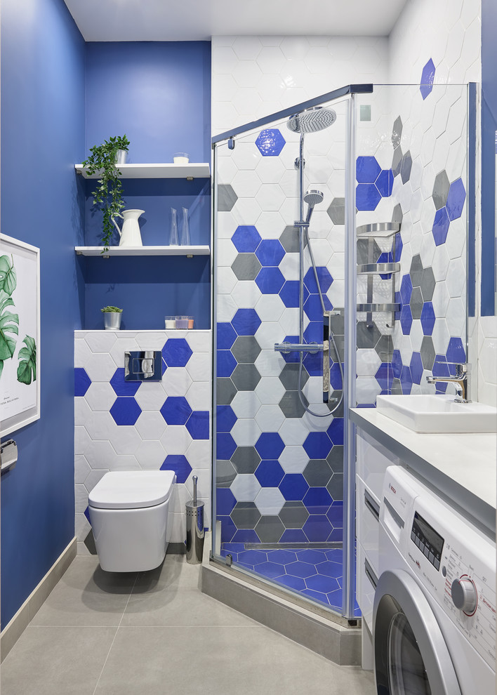 Modern inredning av ett vit vitt badrum med dusch, med släta luckor, vita skåp, en hörndusch, en vägghängd toalettstol, blå kakel, grå kakel, vit kakel, blå väggar, ett nedsänkt handfat, beiget golv och dusch med gångjärnsdörr