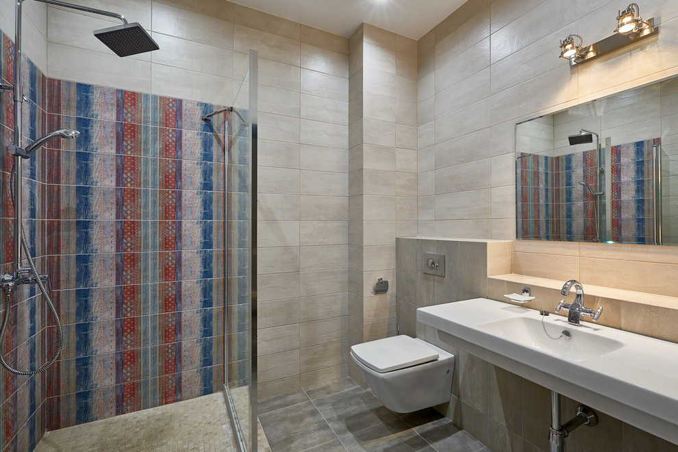 Klassisk inredning av ett badrum med dusch, med en vägghängd toalettstol, beige kakel, flerfärgad kakel, ett väggmonterat handfat, grått golv och med dusch som är öppen