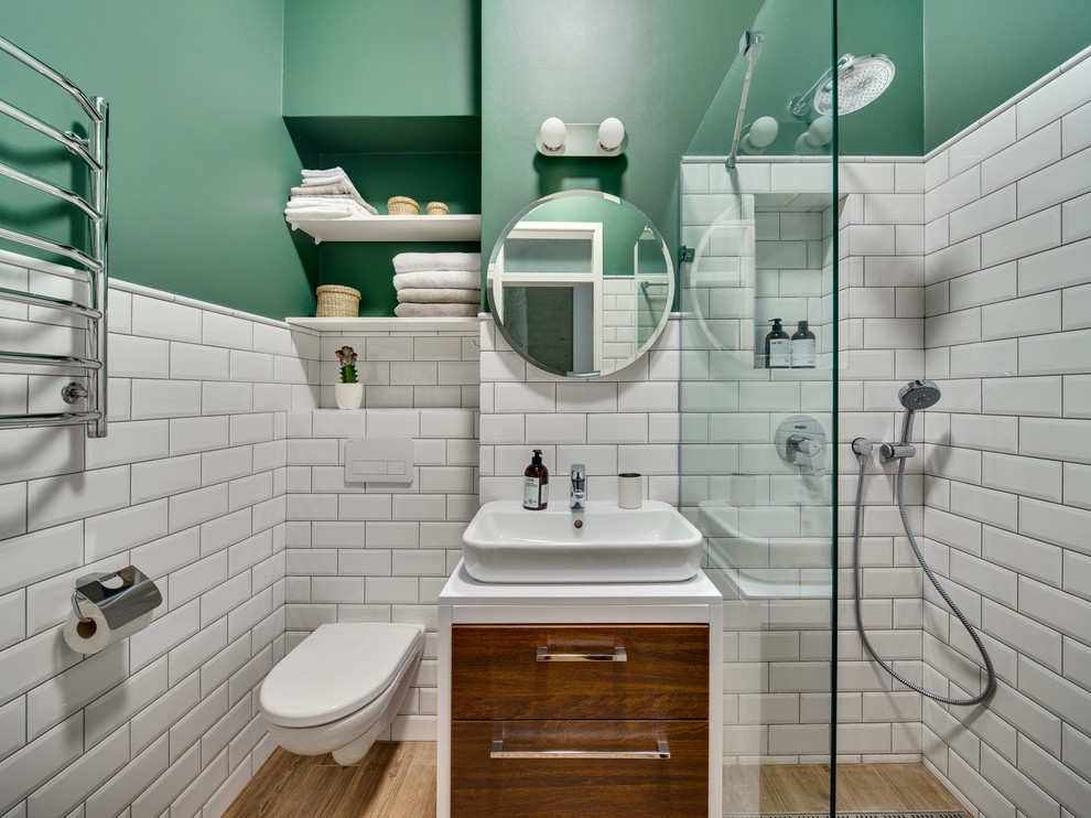 Foto på ett minimalistiskt badrum, med en öppen dusch, en vägghängd toalettstol, vit kakel, tunnelbanekakel, gröna väggar, mellanmörkt trägolv, ett fristående handfat, släta luckor, skåp i mörkt trä och med dusch som är öppen