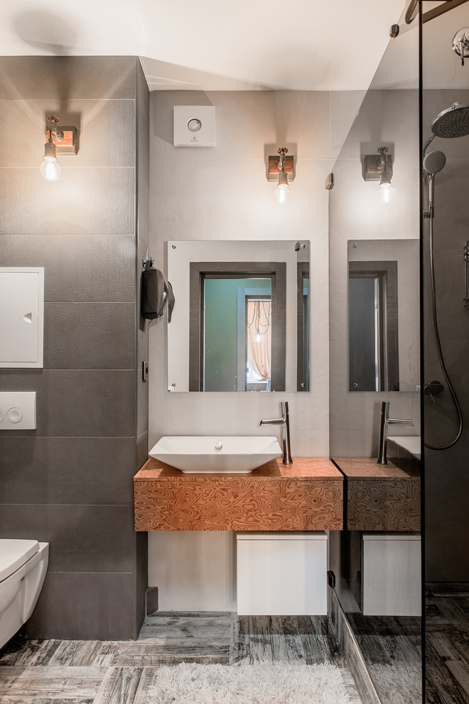Industrial shower room bathroom in Other with an alcove shower, a wall mounted toilet, grey tiles, a vessel sink, grey floors and medium wood cabinets.