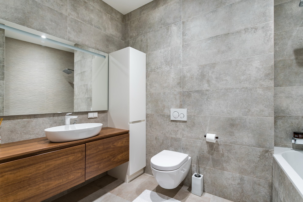 Modern inredning av ett brun brunt badrum med dusch, med släta luckor, skåp i mörkt trä, ett badkar i en alkov, en dusch/badkar-kombination, grå kakel, ett fristående handfat, träbänkskiva och grått golv