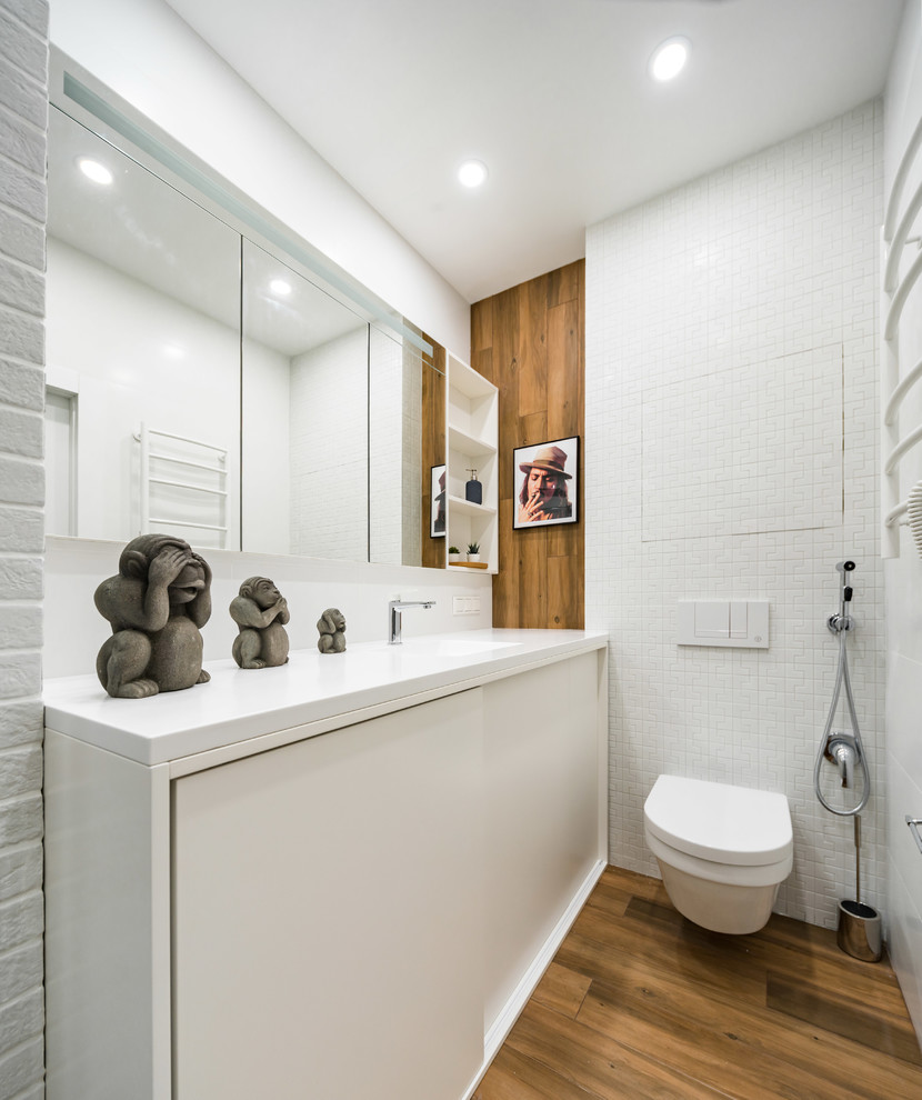 サンクトペテルブルクにあるコンテンポラリースタイルのおしゃれな浴室 (フラットパネル扉のキャビネット、白いキャビネット、壁掛け式トイレ、白いタイル、茶色い床、白い洗面カウンター) の写真
