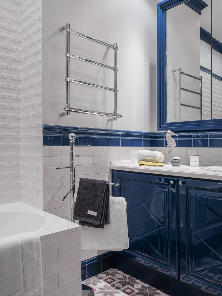 Свежая идея для дизайна: ванная комната среднего размера в стиле неоклассика (современная классика) с синими фасадами, душем над ванной, белой плиткой, керамической плиткой, белыми стенами, полом из керамогранита, накладной раковиной, столешницей из искусственного камня, разноцветным полом, фасадами с выступающей филенкой, накладной ванной, душевой кабиной и открытым душем - отличное фото интерьера
