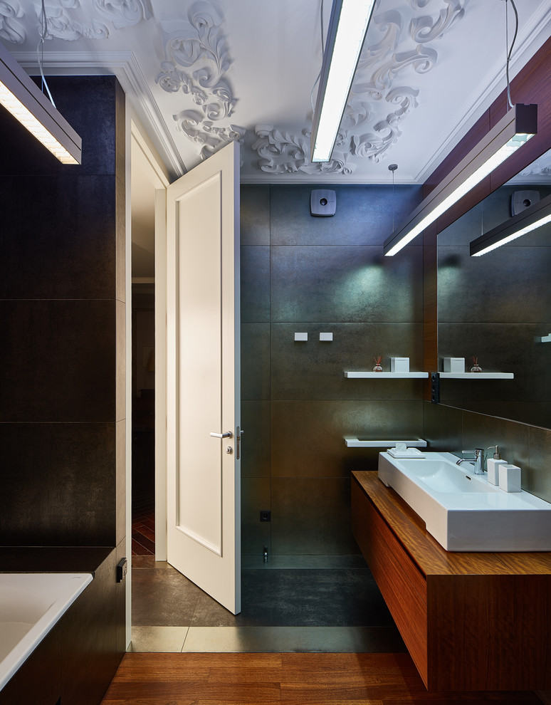 Inspiration pour une salle de bain principale design de taille moyenne avec un placard à porte plane, des portes de placard marrons, une baignoire encastrée, WC suspendus, un carrelage gris, carrelage en métal, un mur gris, un sol en bois brun, une vasque et un plan de toilette en bois.