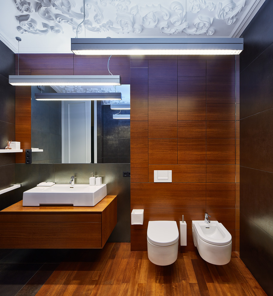 Idée de décoration pour une salle de bain principale design de taille moyenne avec un placard à porte plane, des portes de placard marrons, une baignoire encastrée, WC suspendus, un carrelage gris, carrelage en métal, un mur gris, un sol en bois brun, une vasque et un plan de toilette en bois.