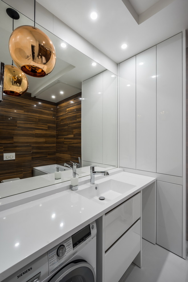 На фото: ванная комната в современном стиле с плоскими фасадами, белыми фасадами, коричневой плиткой, монолитной раковиной и белым полом с
