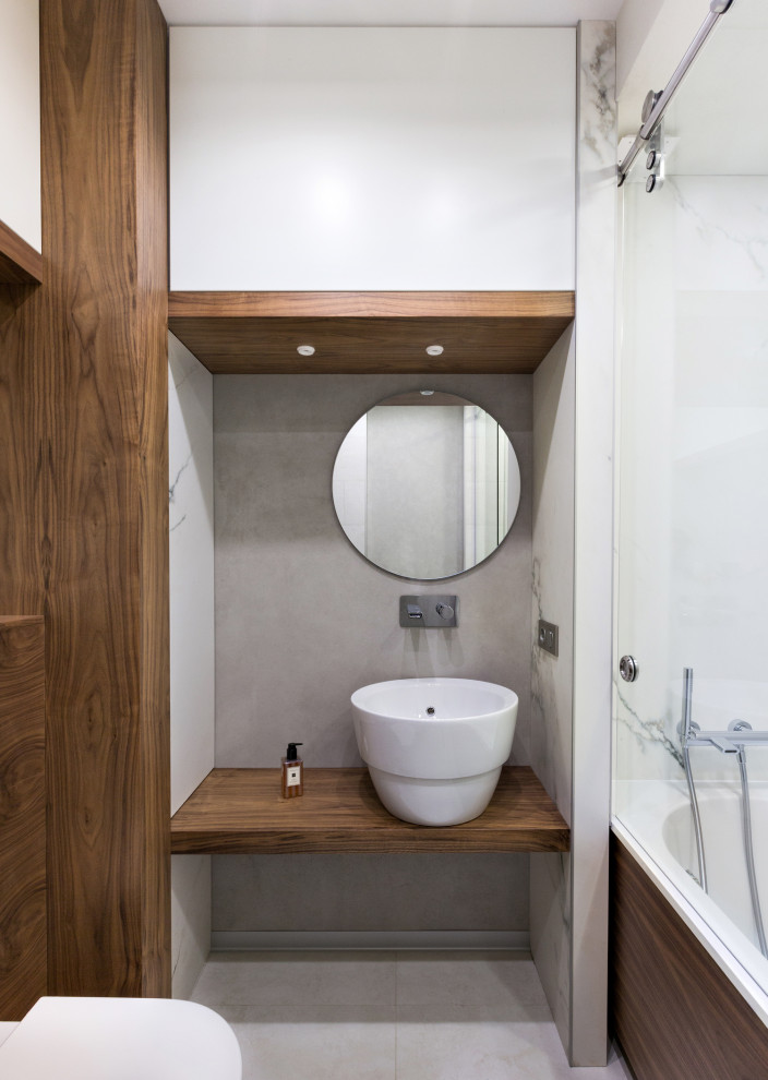 На фото: главная ванная комната в современном стиле с ванной в нише, настольной раковиной, серым полом и коричневой столешницей с