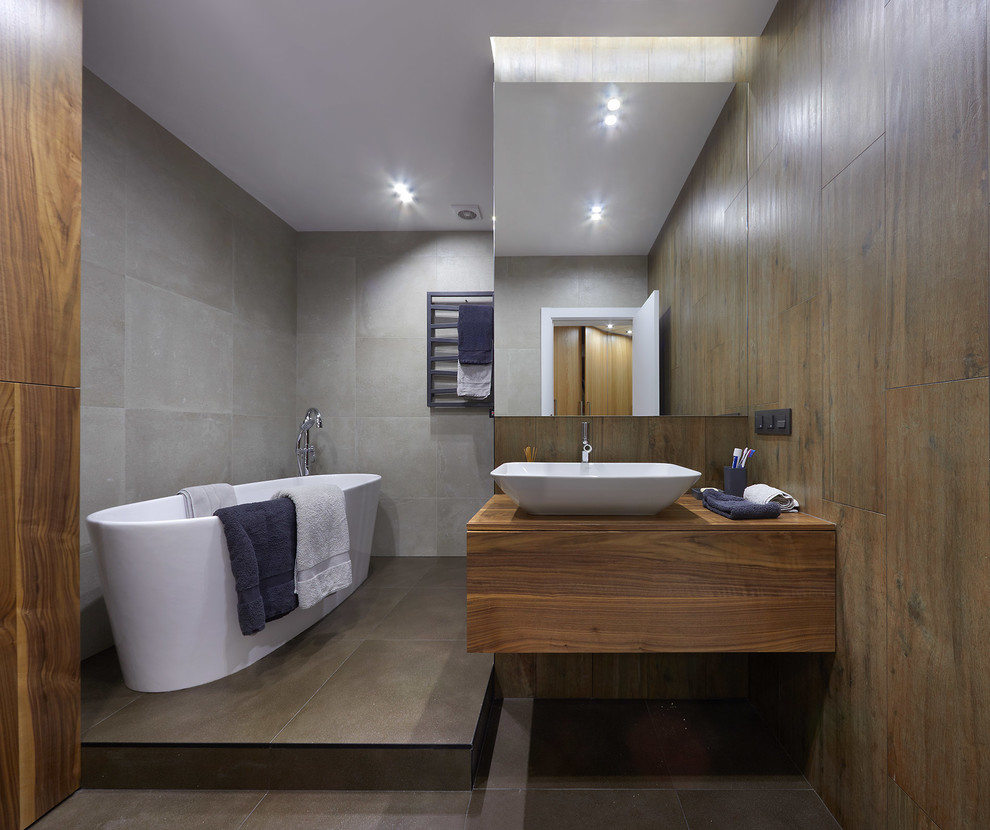 Idéer för att renovera ett funkis brun brunt en-suite badrum, med släta luckor, skåp i mellenmörkt trä, ett fristående badkar, grå kakel, ett fristående handfat, cementkakel, träbänkskiva och grått golv