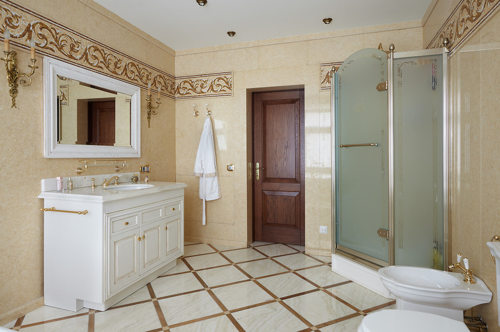 На фото: ванная комната в классическом стиле с фасадами с утопленной филенкой, белыми фасадами, угловым душем, биде, бежевой плиткой, душевой кабиной и врезной раковиной