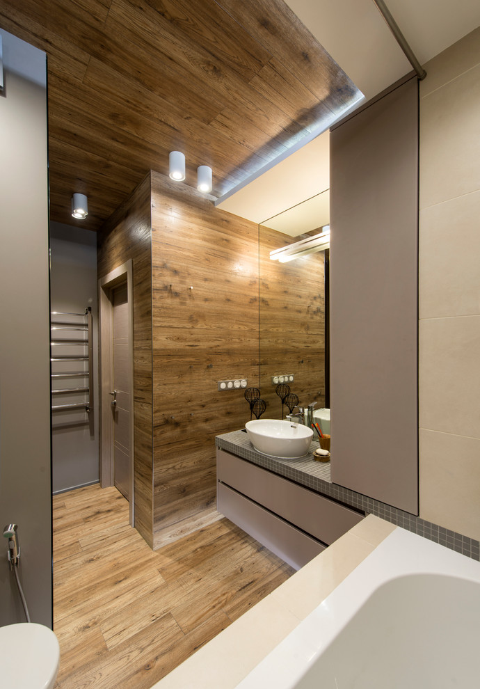 Aménagement d'une salle de bain principale contemporaine avec un placard à porte plane, des portes de placard grises, une vasque, un carrelage beige et un sol en bois brun.