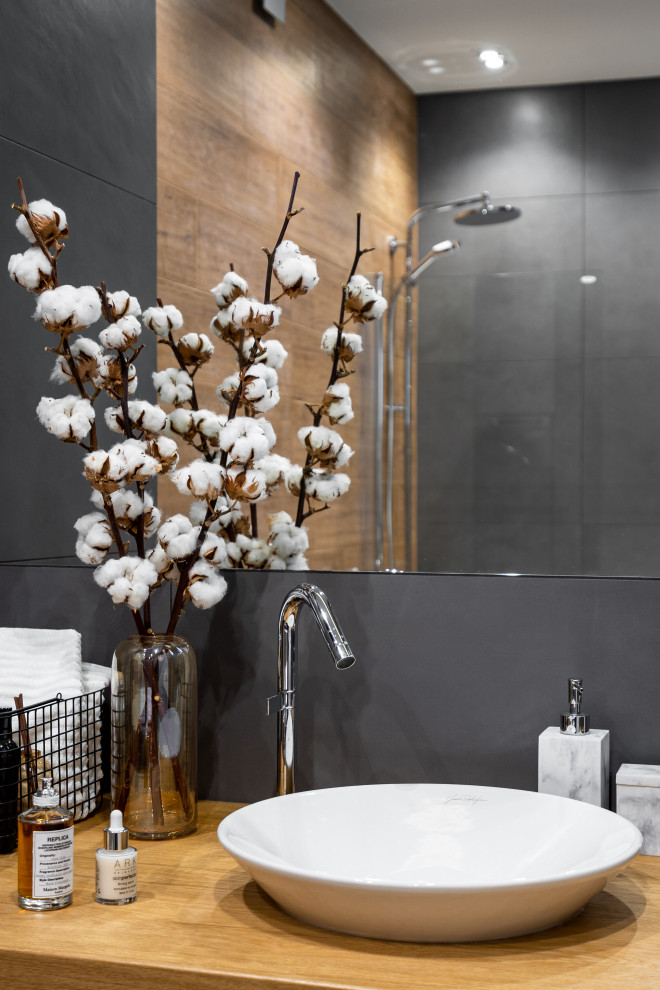 Bild på ett mellanstort funkis en-suite badrum, med släta luckor, skåp i mellenmörkt trä, ett badkar i en alkov, en dusch/badkar-kombination, en vägghängd toalettstol, grå kakel, porslinskakel, grå väggar, klinkergolv i porslin, ett nedsänkt handfat, träbänkskiva, grått golv och dusch med duschdraperi