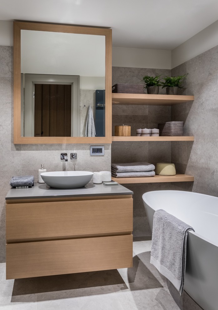Cette photo montre une salle de bain principale tendance en bois brun de taille moyenne avec une baignoire indépendante, un carrelage gris, du carrelage en marbre, un sol en marbre, une vasque, un sol gris, un placard à porte plane et un plan de toilette gris.