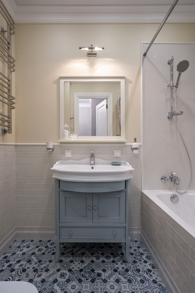 Cette image montre une salle d'eau traditionnelle avec des portes de placard bleues, une baignoire en alcôve, un combiné douche/baignoire, un carrelage blanc, un mur beige, un sol en carrelage de céramique, un lavabo intégré, un sol multicolore, une cabine de douche avec un rideau, du carrelage bicolore et un placard à porte shaker.