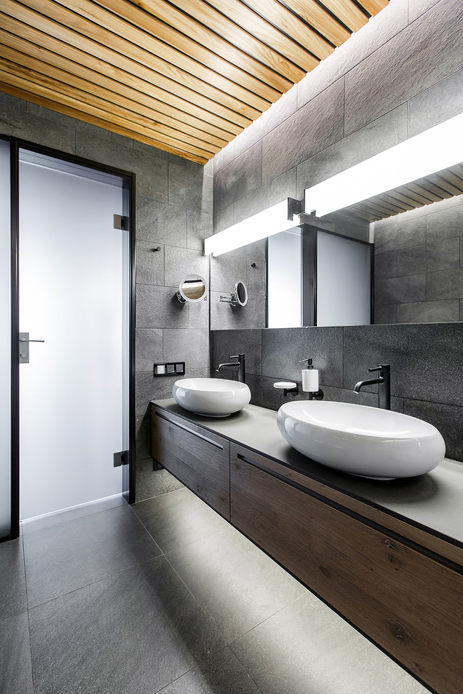 Пример оригинального дизайна: ванная комната в современном стиле с плоскими фасадами, серой плиткой, настольной раковиной, фасадами цвета дерева среднего тона и зеркалом с подсветкой