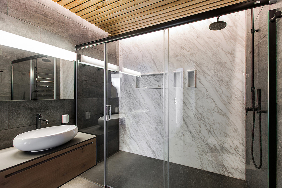 Aménagement d'une salle de bain contemporaine en bois brun avec un placard à porte plane, un carrelage noir, un mur multicolore et une vasque.