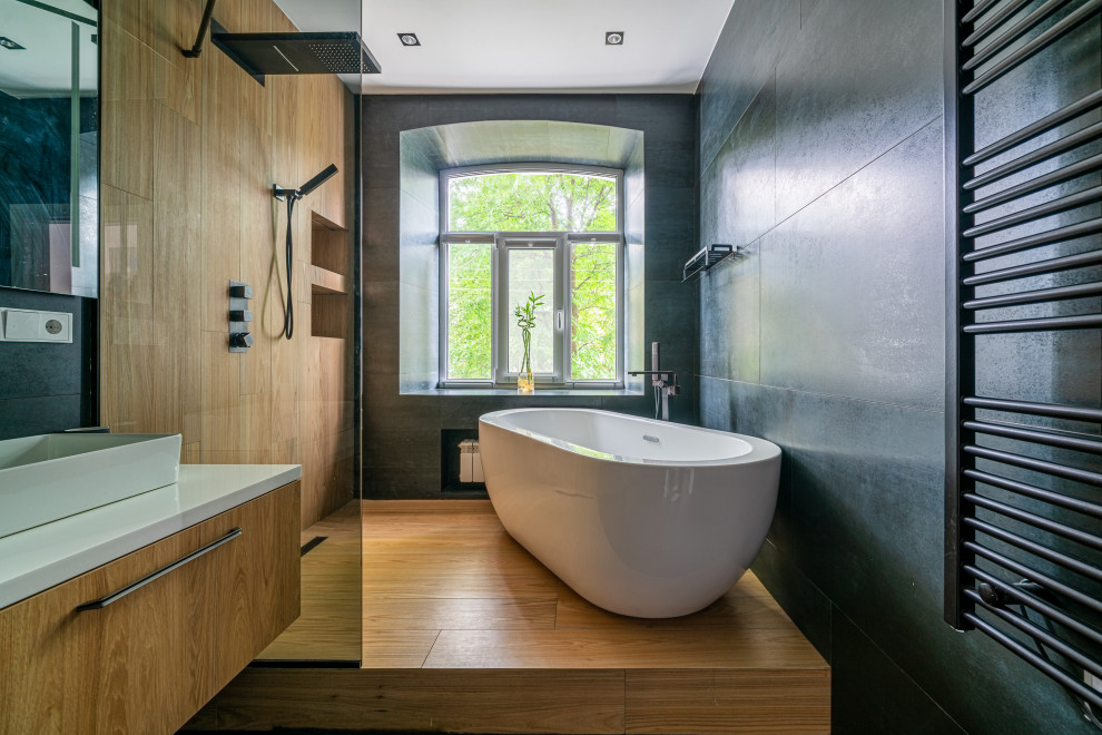 Foto på ett funkis vit badrum, med släta luckor, skåp i mellenmörkt trä, ett fristående badkar, svart kakel, mellanmörkt trägolv, ett fristående handfat och brunt golv