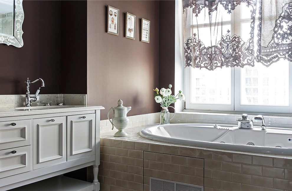 На фото: главная ванная комната в классическом стиле с фасадами с утопленной филенкой, белыми фасадами, гидромассажной ванной, бежевой плиткой, коричневыми стенами, врезной раковиной и мраморной столешницей с