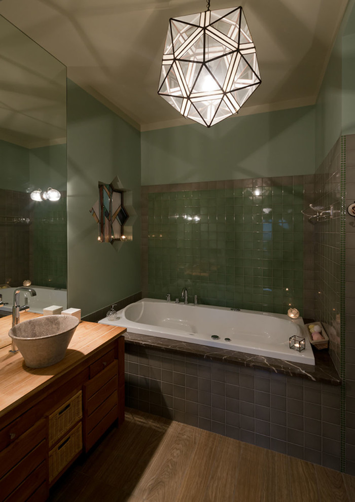 Пример оригинального дизайна: главная ванная комната среднего размера в стиле фьюжн с искусственно-состаренными фасадами, гидромассажной ванной, зеленой плиткой, керамической плиткой, зелеными стенами, полом из керамогранита, столешницей из дерева и настольной раковиной