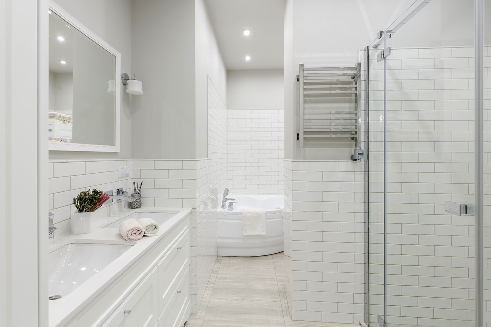 Стильный дизайн: большая главная ванная комната в стиле неоклассика (современная классика) с угловой ванной, угловым душем, белой плиткой, плиткой кабанчик, серыми стенами, врезной раковиной, столешницей из искусственного кварца, душем с распашными дверями, белой столешницей, фасадами с утопленной филенкой, белыми фасадами и серым полом - последний тренд